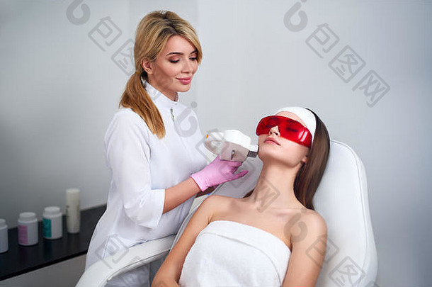 美容师医生在美容院为迷人的年轻女子进行激光射频<strong>嫩肤</strong>。Elos美容脱毛程序。美容面部