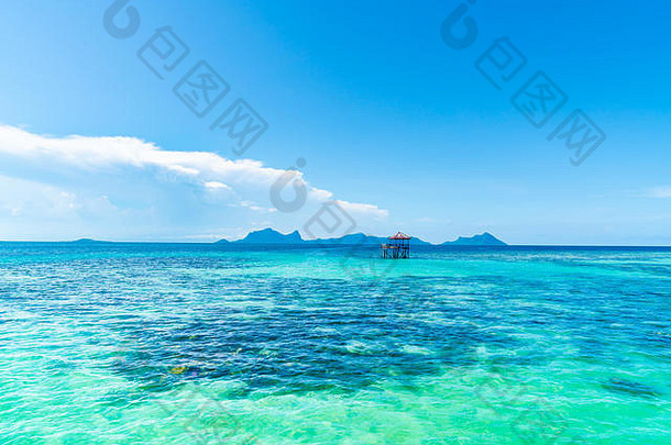 热带背景绿松石色的大海和蔚蓝的天空，远处的岛屿在地平线上，一个小结构在海中央的高跷上。
