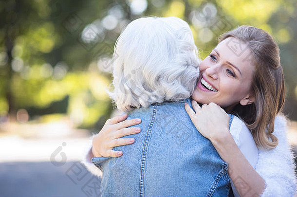 快乐年轻的女人拥抱退休妈妈。公园