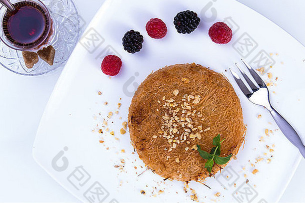 土耳其甜点kunefe装在白色盘子里，上面有薄荷叶和草莓片，还有红色和黑色的浆果