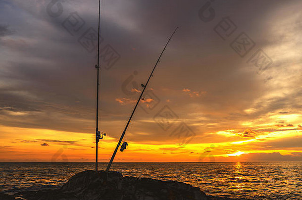 钓鱼杆的背景是美丽的橙色夕阳在海上。普吉岛，考湖。傍晚