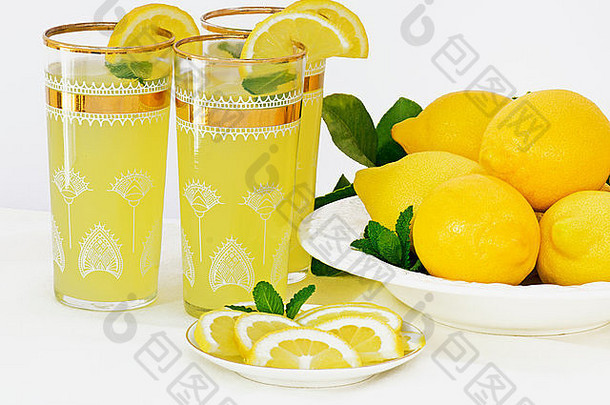 柠檬水加薄荷的冰冷饮，装在金色镶边的玻璃杯中，旁边是一盘新鲜采摘的柠檬和柠檬皮