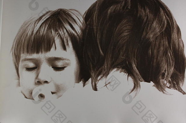 20世纪70年代，一位白人女孩把头靠在母亲的肩膀上吮吸奶嘴，这是一张精美的黑白艺术照片。