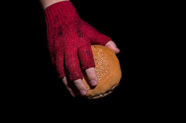 贫困概念。戴着脏手套的手拿着隔离在黑色背景上的面包。