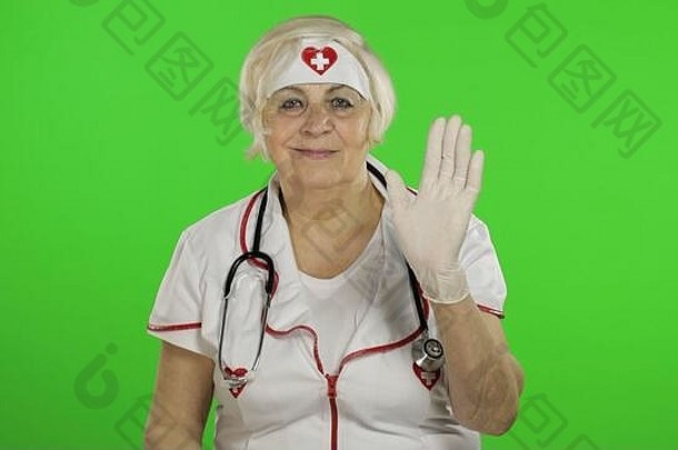 戴着医学面具的老年白人女医生的肖像。女护士。她挥舞着双手。打个招呼。病毒防护。流行病冠状病毒。2019冠状病毒疾病绿色屏幕。色度键