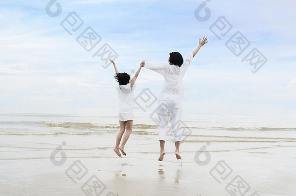 暑假期间放松亚洲家庭时光。亚洲妈妈和女儿手牵着手，在沙滩上嬉戏玩耍。