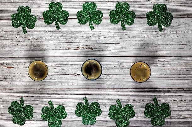 在木质背景上用三叶草叶子和啤酒杯构成的平铺构图。圣帕特里克节