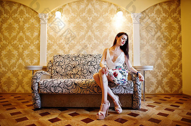 一位穿着<strong>花裙子</strong>和高跟鞋坐在金色房间沙发上的神奇年轻女子的肖像。