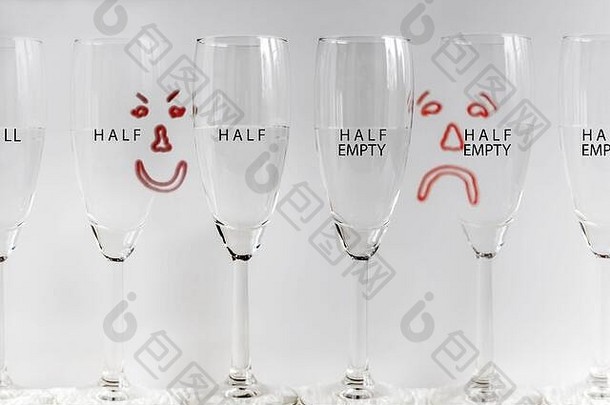 六个酒杯，半满，背景中绘有悲伤和快乐的面孔，描绘了酒杯半满或酒杯半空的概念。
