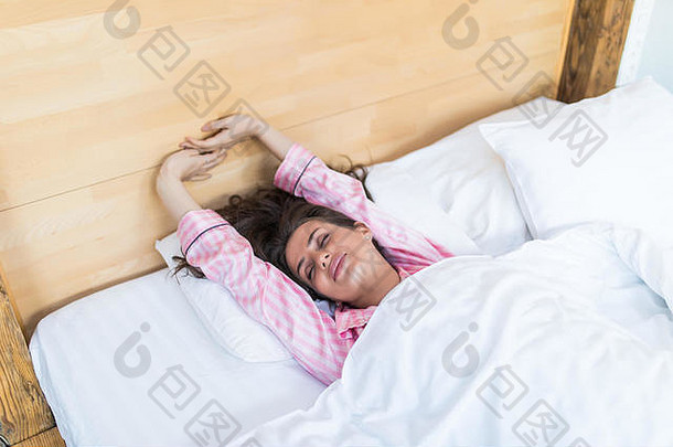 年轻的微笑的美丽女士躺在室内的床上。闭上眼睛。