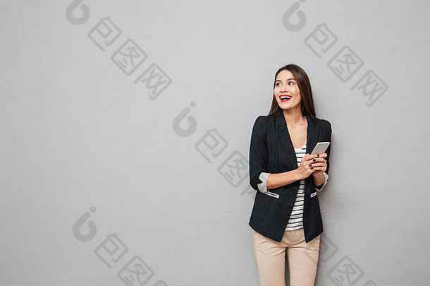 快乐的亚洲业务女人持有智能手机灰色的背景