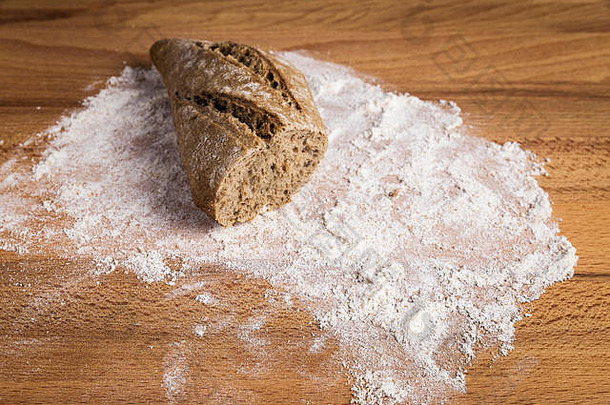 在木桌上的面粉上拉长的一小块全麦面包