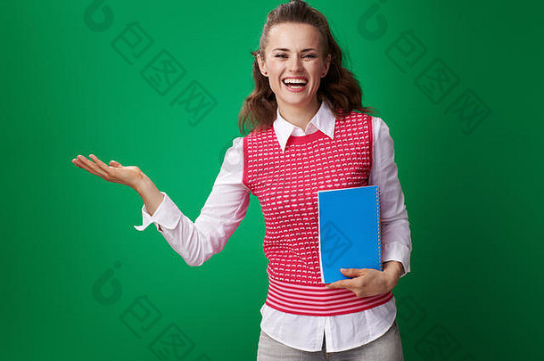微笑的现代女学生穿着红色马甲，蓝色笔记本，在绿色的空手掌上展示着一些东西