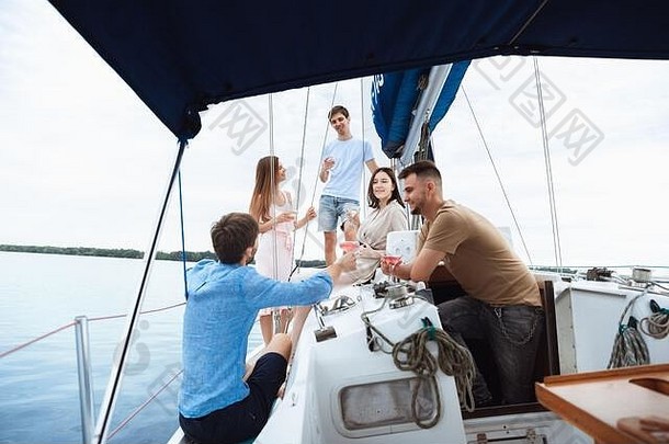 一群快乐的朋友在户外的船上聚会上喝着伏特加鸡尾酒，兴高采烈。年轻人享受海游、青春和暑假的乐趣。喝酒、度假、休息。