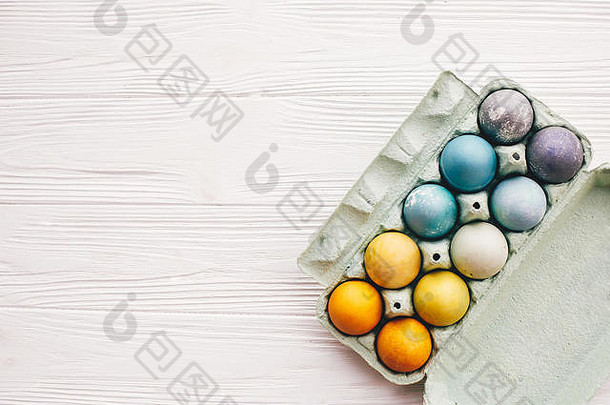 白色木质背景的纸盒托盘中的时尚复活节彩蛋，俯视图。用不同颜色的天然染料绘制的现代彩色复活节彩蛋。羟基磷灰石