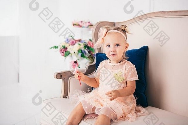2岁的有趣女孩穿着粉色公主裙坐在家里吃蛋糕。主题是儿童节。儿童天然糖果。糖尿病与疾病