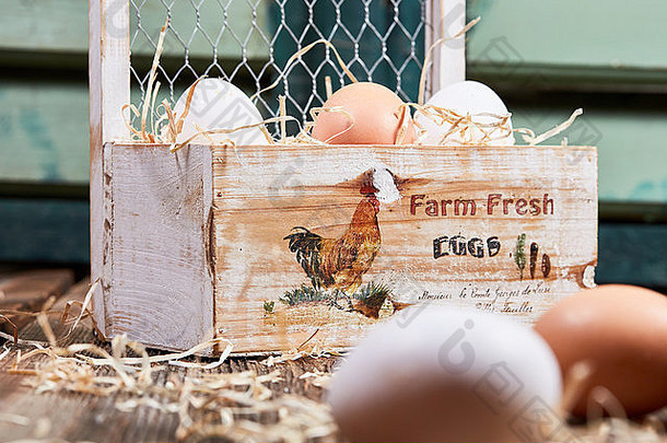 新鲜的农场鸡蛋和稻草放在绿色窗户前的木箱里
