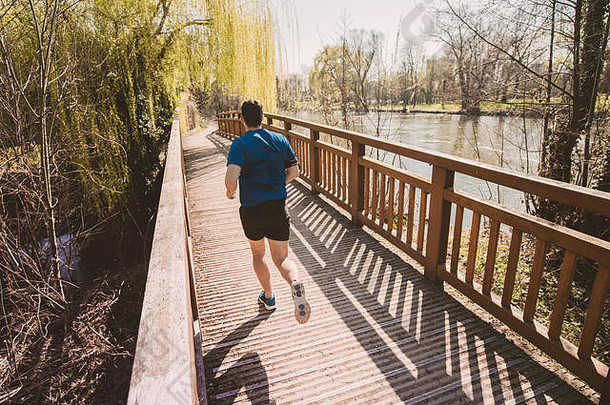 后视图：一名男子跑步者在城市公园里跑过桥，进行体能训练。健康生活方式理念。训练慢跑活<strong>动</strong>，<strong>动</strong>感跑步者