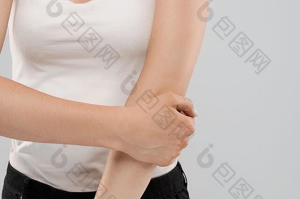 一名身穿白衬衫的不知名白人妇女在灰色隔离背景上摆姿势，因受伤而触摸肘部。手臂疼痛的黑发女人的前腰。