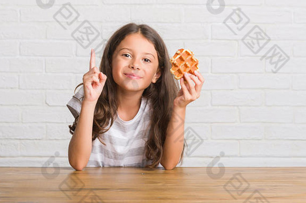 年轻的拉美裔孩子坐着表格吃华夫格惊讶的想法问题指出手指快乐脸数量
