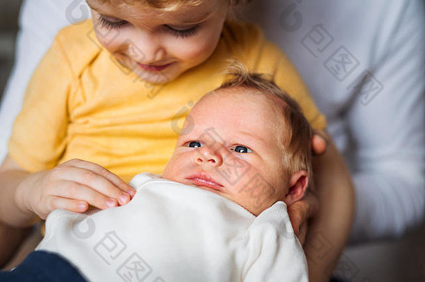 一个小男孩在家里抱着一个刚出生的弟弟。