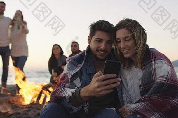 情侣们在沙滩派对上用手机和朋友们一起喝啤酒，玩得很开心