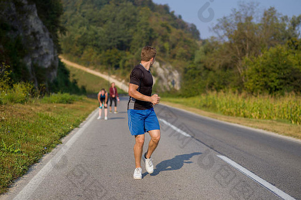 一群年轻人在乡村公路上慢跑，在夏天的一天在开阔的公路上跑步