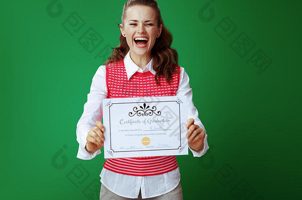 身着灰色牛仔裤和粉色无袖衬衫的年轻女学生面带微笑，在黑板绿色背景下展示毕业证书。