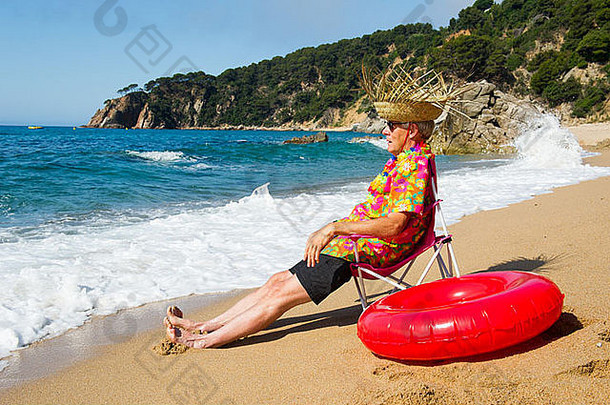 夏日海滩上坐在椅子上拿着玩具的老人