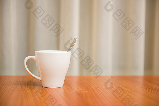 木桌上的带勺子的白色马克杯。