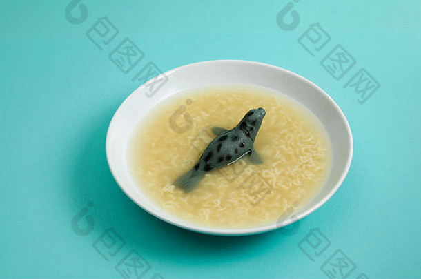 一种海狮动物在带有字母意大利面的肉汤中游泳。古怪、有趣、色彩简约的静物摄影