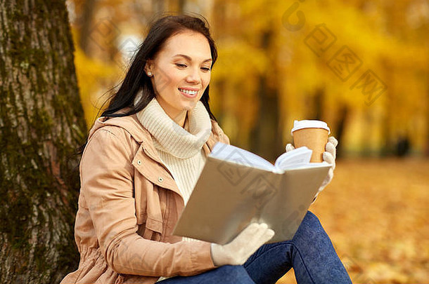 秋天公园里，一个女人一边喝咖啡一边看书