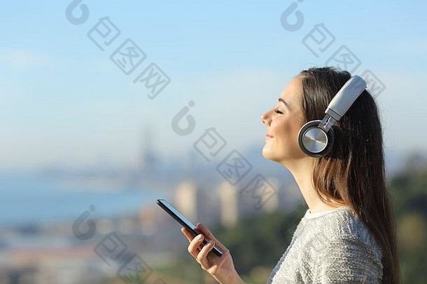 一边视图肖像满意女孩听音乐穿耳机持有移动电话在户外城市郊区