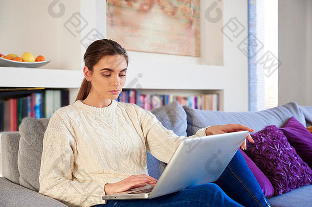 在家工作时在笔记本电脑上打字的美丽年轻女子的肖像。
