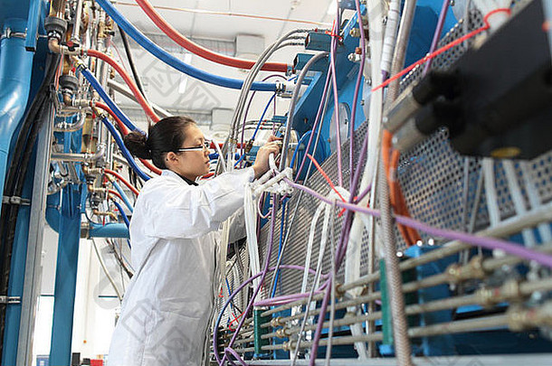 一位在实验室工作的亚洲女科学家穿着实验室外套，身上有很多电缆