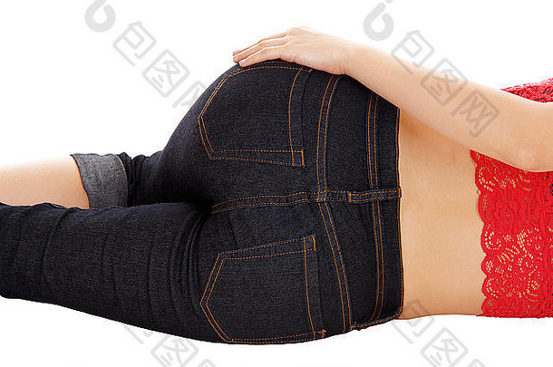一个穿着牛仔裤躺在地板上的年轻女子的屁股，手放在臀部，白色背景隔离。