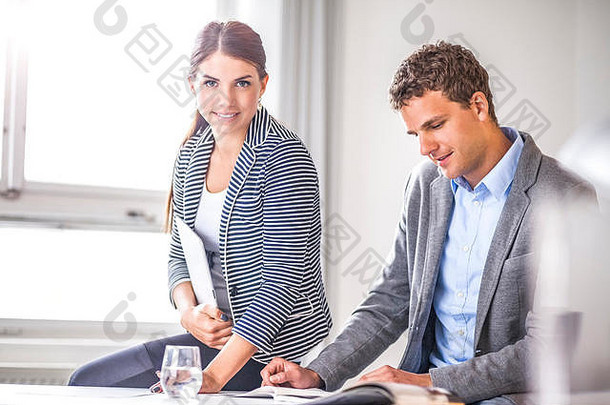 年轻女商人坐在男同事旁边阅读办公室宣传册的照片