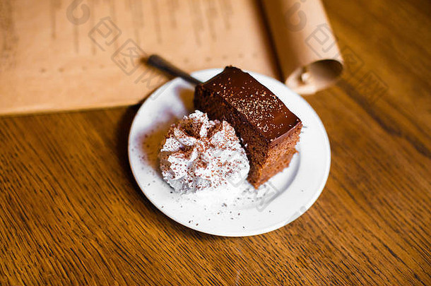 一块黑巧克力馅饼放在<strong>鲜奶</strong>油旁边，上面装饰着巧克力，放在工艺菜单旁边。侧视图。