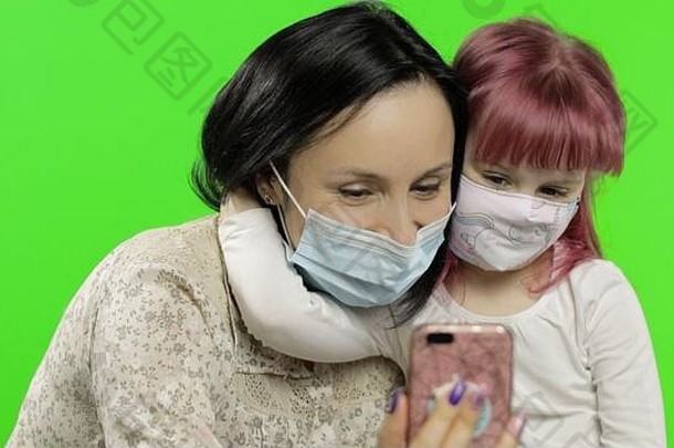 母亲、女儿戴着口罩，手持<strong>手机</strong>在视频通话。C2019冠状病毒疾病的社会疏远保护概念可爱的小孩喜欢使用智能<strong>手机</strong>。社会化媒体。色度键