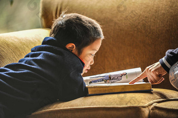 一个小男孩坐在沙发上看一本大图画书。母亲<strong>的</strong>指指点点。特写、自然光、水平、非姿势