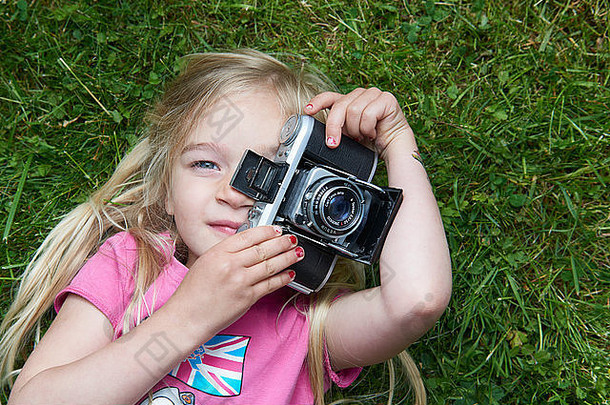 小女孩躺在草地上，用老式复古胶卷相机拍照的肖像