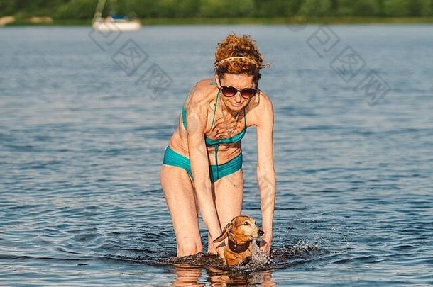 迷人的成熟女人喜欢在夏天和她的狗在捕鲸场玩耍。夏天和生活方式。达克斯猎犬在河里游泳。老人