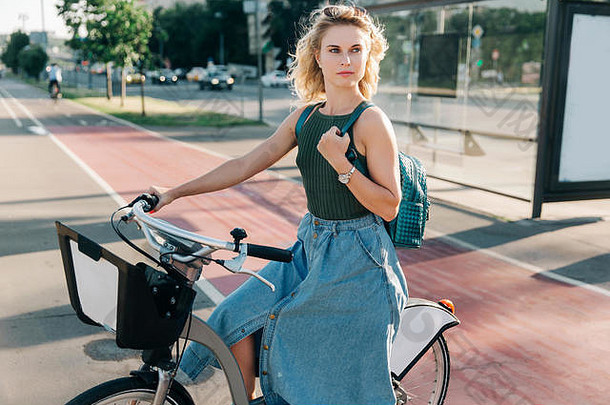 一位金发女郎坐在公共汽车站附近的自行车上的照片