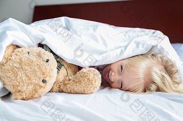 可爱的金发小女孩和玩具熊躺在床上。快乐的童年。COVID-2019冠状病毒疾病的家中滞留