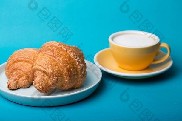 法式早餐。美丽的咖啡黄杯卡布奇诺，蓝底牛角面包