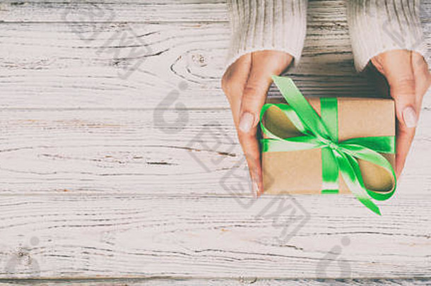 女士亲手送包装好的情人节礼物或其他节日手工制作的礼物，用绿色丝带做成。礼品盒，木制桌子上的礼品装饰，顶部