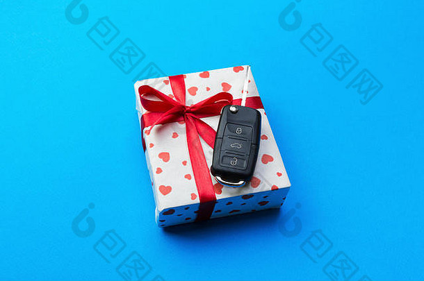 带红色丝带蝴蝶结的纸质礼品盒上的车钥匙和蓝色桌子背景上的心形钥匙。假日呈现顶视图概念。