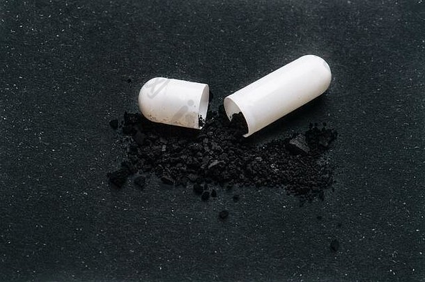 打开的药物胶囊，黑色粉末成分撒在附近表面