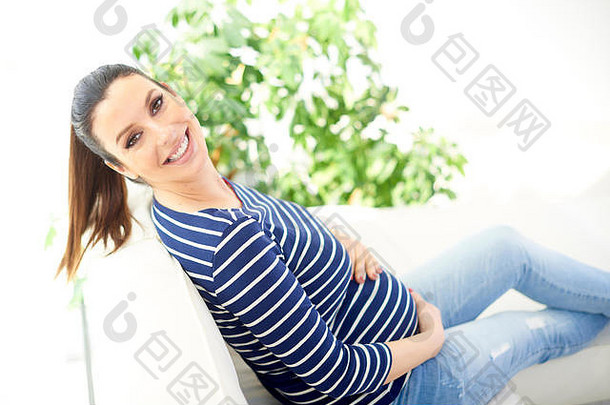 高角度拍摄的美丽孕妇双手抱着婴儿，在家里的沙发上休息时撞到了怀孕的额约因。