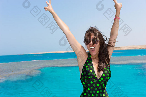 女人<strong>墨绿</strong>色泳衣提高手笑游艇阳光明媚的夏天一天美丽的绿松石海背景